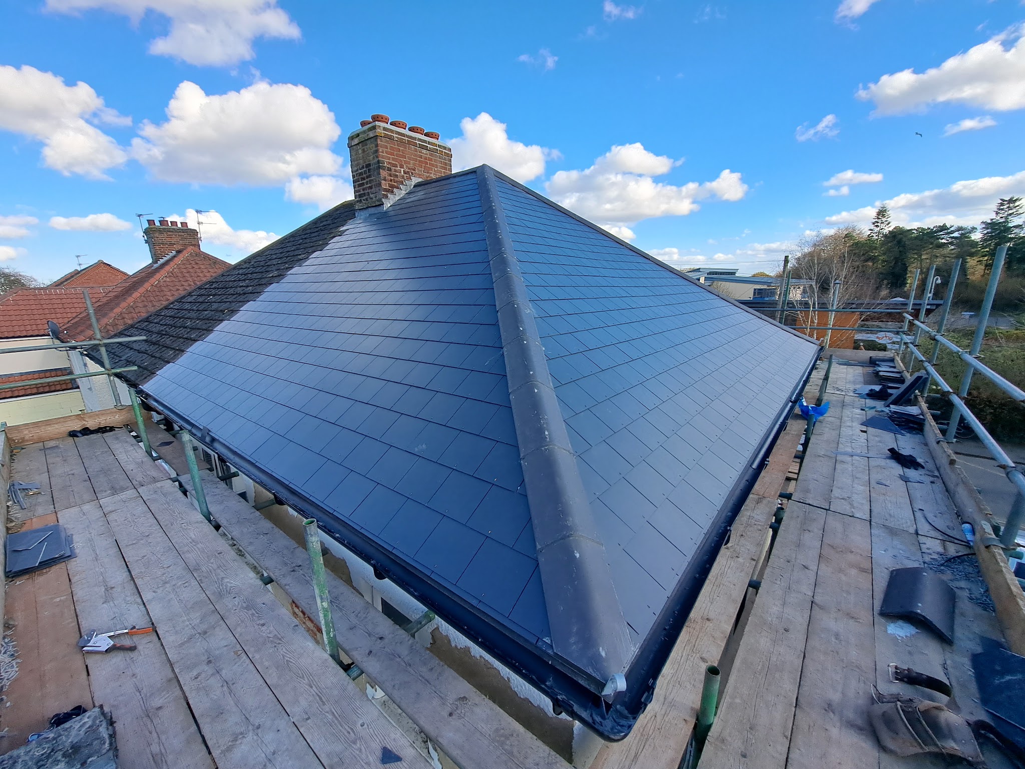 A new hipped roof in dark slate, seen from the scaffold