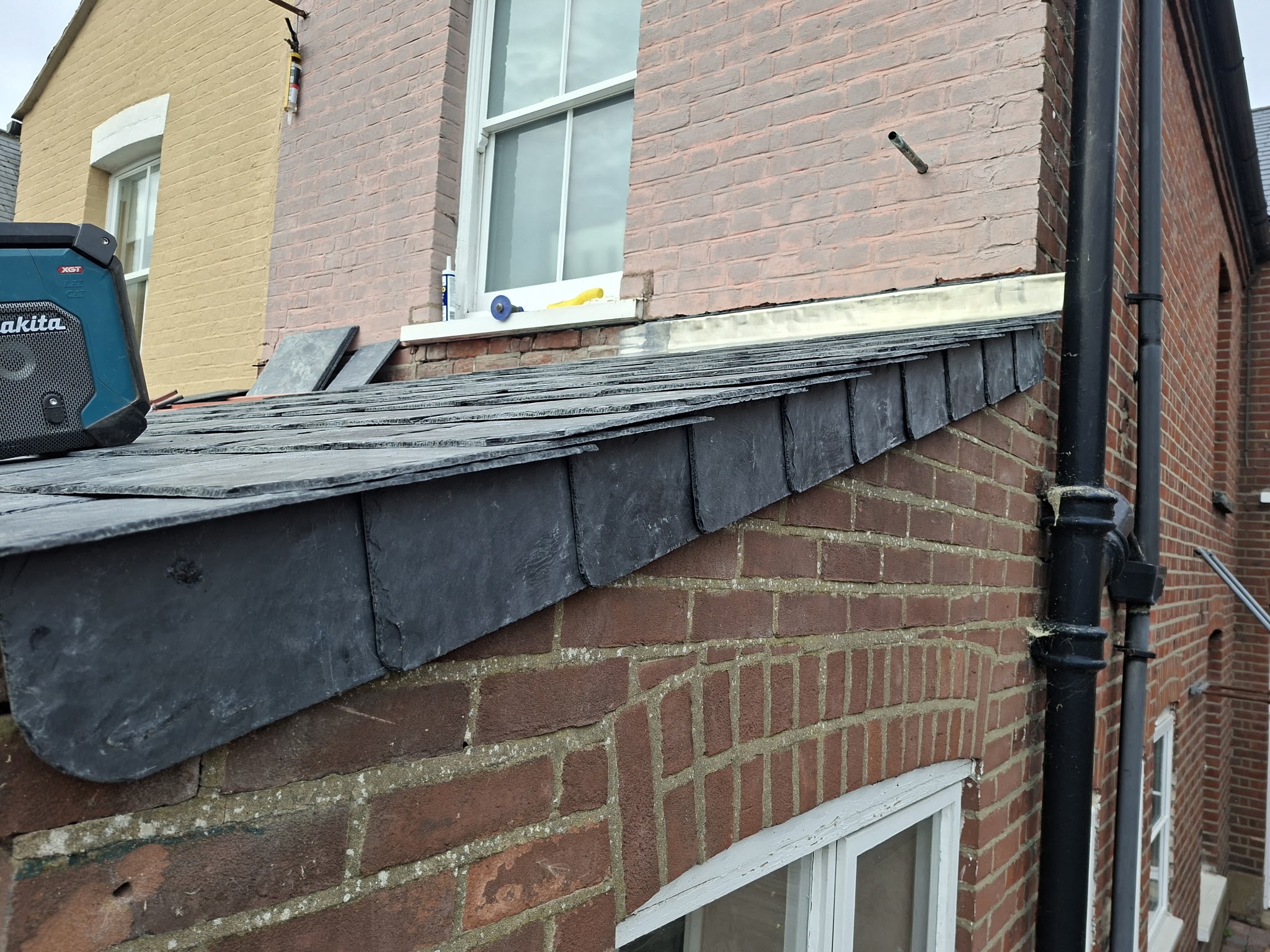 A slate lean-to roof edge against a red brick wall