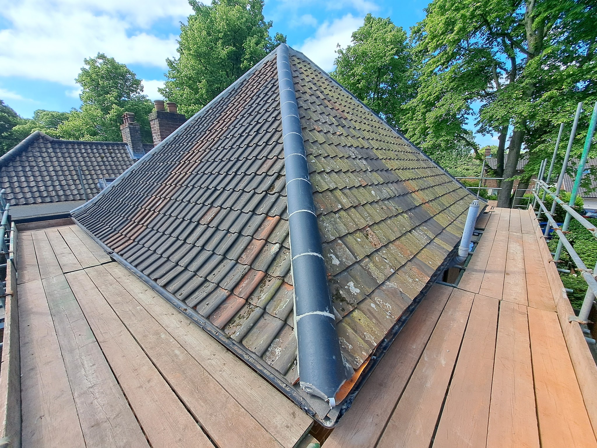 A hipped plain clay tile roof with a new ridge, from the scaffold walkway
