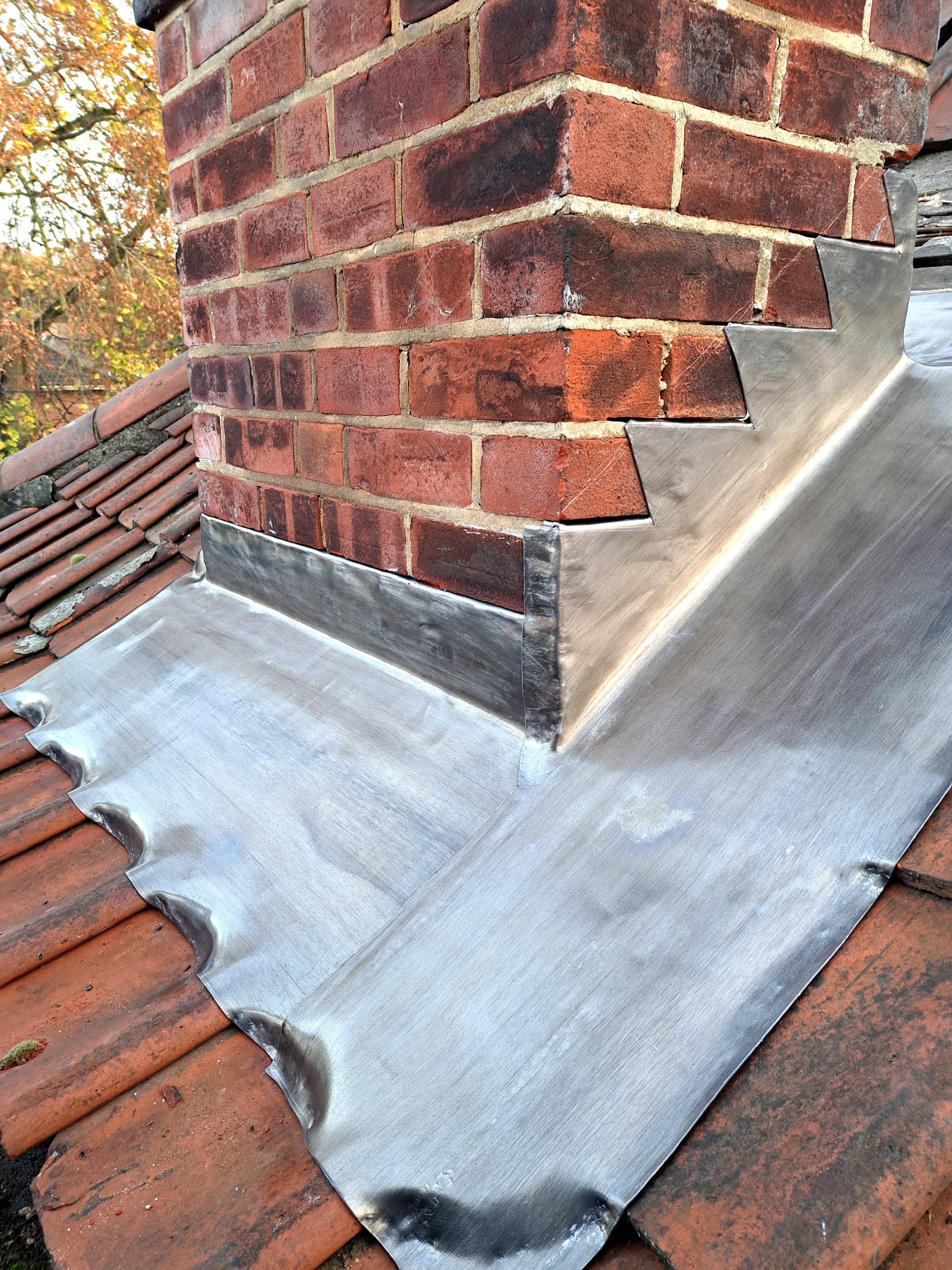 New lead flashing stepped around a brick chimney on a clay pantile roof